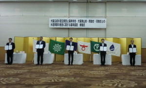 関係者の方々5名が等間隔に間をあけ、それぞれ協定書を持って記念撮影をしている写真