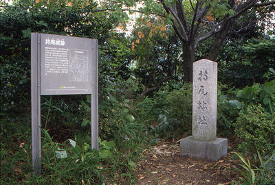 木々や草むらの中にある城跡碑と説明板が設置された持尾城跡の写真
