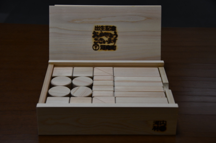 木製の箱の中に形の違う積み木が収められ、蓋の表中央に出生記念おめでとうございますの文字が焼き印がされている出生記念木製玩具の写真