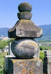 丸い石と家の屋根の形の石が重なった、墓全体を見守る五輪塔の写真