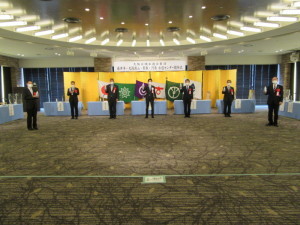 金屏風が置かれた会場で関係者7名が間隔をあけて立ち記念撮影をしている写真