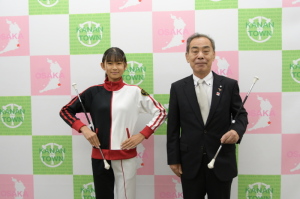 右手でバトンを持ち、左手を腰に添えている林さんと、左手にバトンを持った森田町長が記念撮影をしている写真