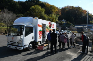 トラックの荷台部分に野菜のキャラクターのようなものが描かれている移動販売車を視察している関係者たちの写真