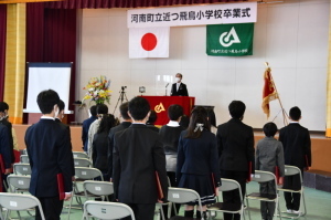 並べられたパイプ椅子の前に立ち、ステージ上で話をしている町長の話を聞いている卒業生たちの後ろ姿の写真