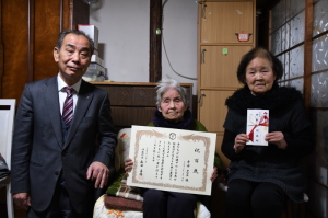 賞状を持った寺田さんと、お祝いを持っている寺田さんのご家族、森田町長が一緒に記念撮影をしている写真