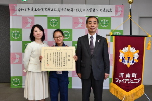 賞状を持った女の子、女の子の左横に立っている女性、女の子の右側に立っている森田町長3人で記念撮影をしている写真