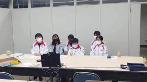 白を基調としたジャージを着た河南町ファイヤジュニアの方6名がテーブルの上に置かれたパソコンの前に座り、事前打ち合わせをしている写真