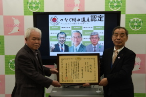 「つなぐ棚田遺産認定」と書かれ3名の男性の顔が映し出されたモニターの前で平石棚田保存会の木田さんと森田町長が一緒に賞状を持ち記念撮影をしている写真