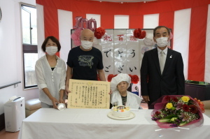 紅白幕が張られた室内で森田町長、山本さん、山本さん家族が記念撮影をしている写真