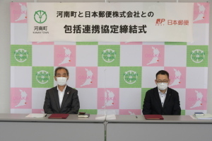 締結式にて森田町長と、松阪河南郵便局長がテーブルに座り正面を見ている写真
