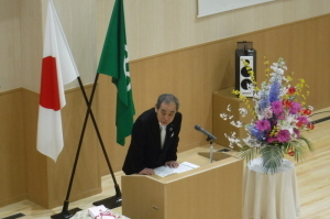 中村こども園開園式入園式にて、花が飾られた横の演台で話をしている町長の写真
