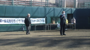 「第47回河南町老人クラブ連合会グラウンド・ゴルフ大会」と書かれた横断幕があるグラウンドで、町長がマイクを持ち話をしている様子の写真
