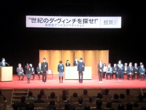 「“世紀のダ・ヴィンチを探せ！」授賞式の会場で、受賞者の高校生が舞台上に並んで立っている授賞式の様子の写真