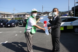 古川代表と森田町長が一緒に赤い花のリボンがついた大きなカギの模型を持っている車両引渡し式の写真