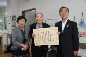 左から女性、賞状を持った高齢の男性、森田町長が横一列に並んで記念撮影をしている写真