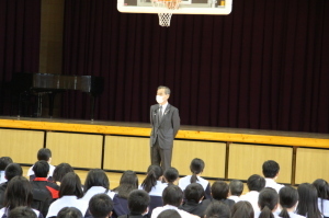 体育館で床に座っている生徒達の前で挨拶をしている森田町長の写真