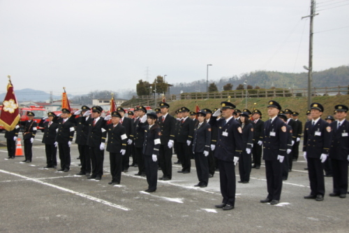 消防団員の人達が制服姿で整列し、前列の人たちが敬礼をしている出初式の写真