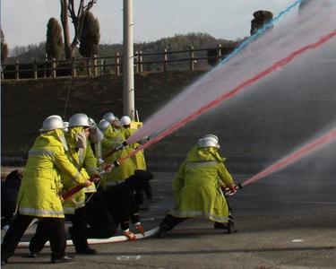 出初式で赤や水色の水を放水している消防団員を横から写した写真